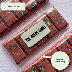 Three bars of pink cherry-scented wax melts in clear plastic packaging, decorated with colorful glitter, with a paper label reading 'THE SCENT LABEL'.