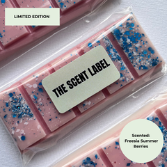 Three pink wax melts in clear plastic packaging with blue and white glitter, featuring a central label that reads 'THE SCENT LABEL' and a circular badge that says 'Scented: Freesia Summer Berries'.