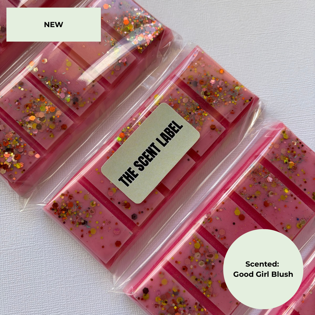 Three pink scented wax melts in clear plastic packaging arranged diagonally on a white textured background. Each package has a cream-colored label, with the center label reading 'THE SCENT LABEL'.